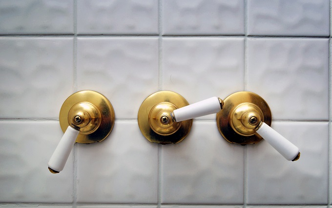 Three golden shower valve handles on a big white empty tile shower room