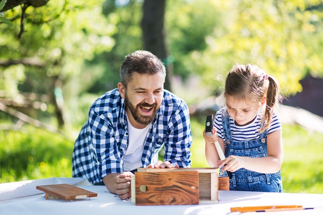 Father with a small daughter outside, making wooden birdhouse.