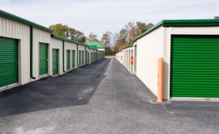 New outdoor mini storage warehouse buildings with green doors and an empty parking lot.
