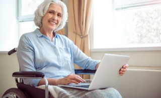 Digitalization. Cheerful and positive senior woman in wheelchair using laptop