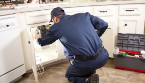 HVAC maintenance man works under the sink near the dishwasher.