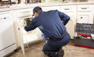 HVAC maintenance man works under the sink near the dishwasher.