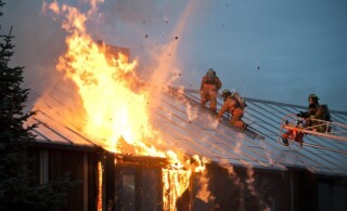 Fire fighters on roof of a home in flames