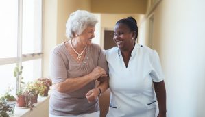 Smiling home caregiver and senior woman walking together