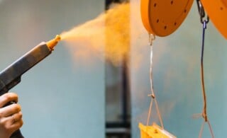 Powder coating of metal parts. A man in a protective suit sprays powder paint from a gun on metal products.