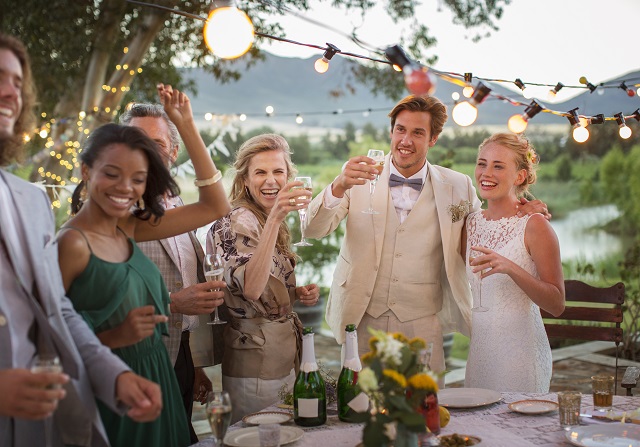 Young couple and guests toasting with champagne during wedding reception in backyard