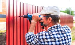 Man in plaid shirt and hat screws a vinyl fence board into a post