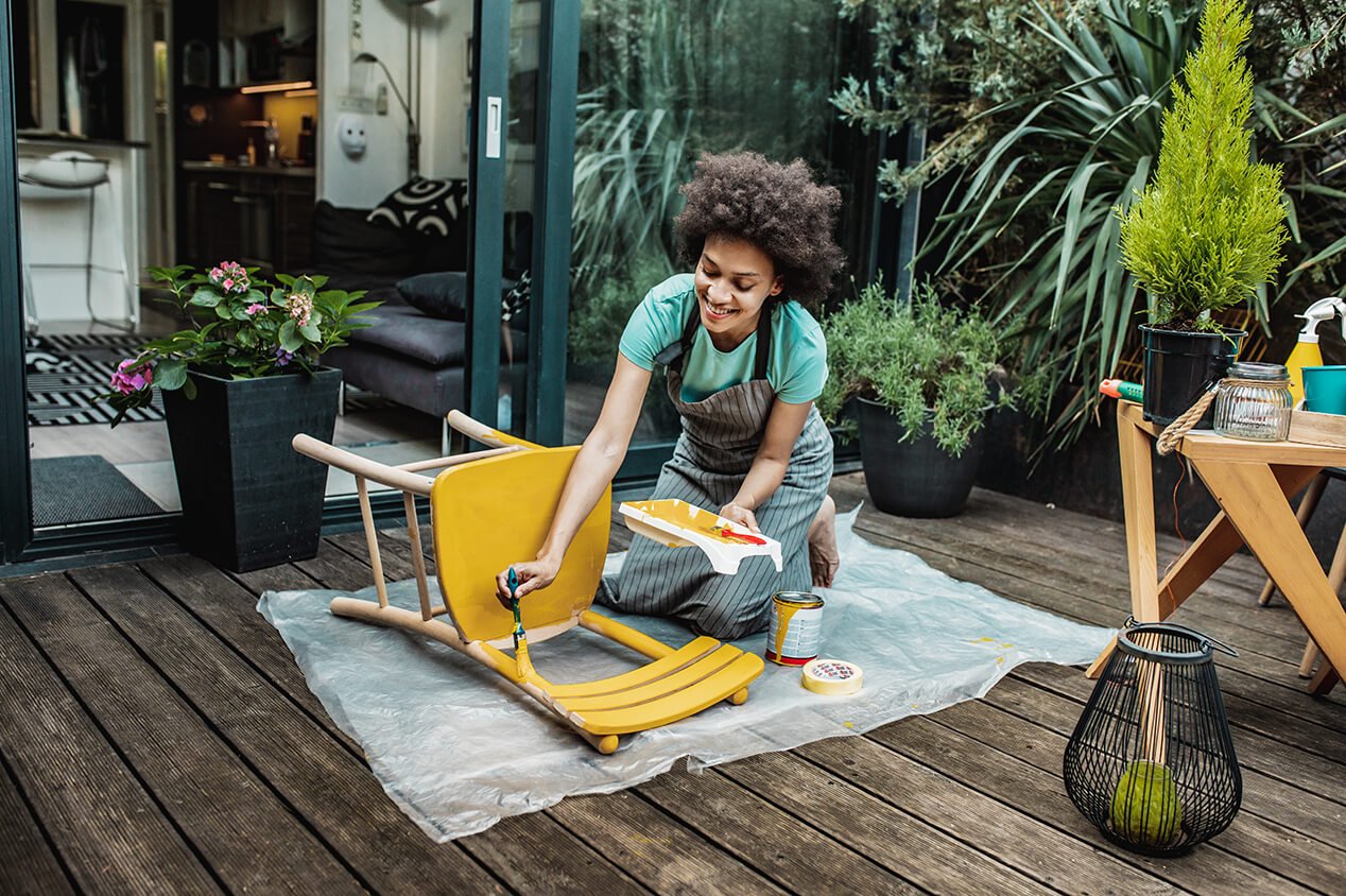 Young woman repainting wooden chair on patio