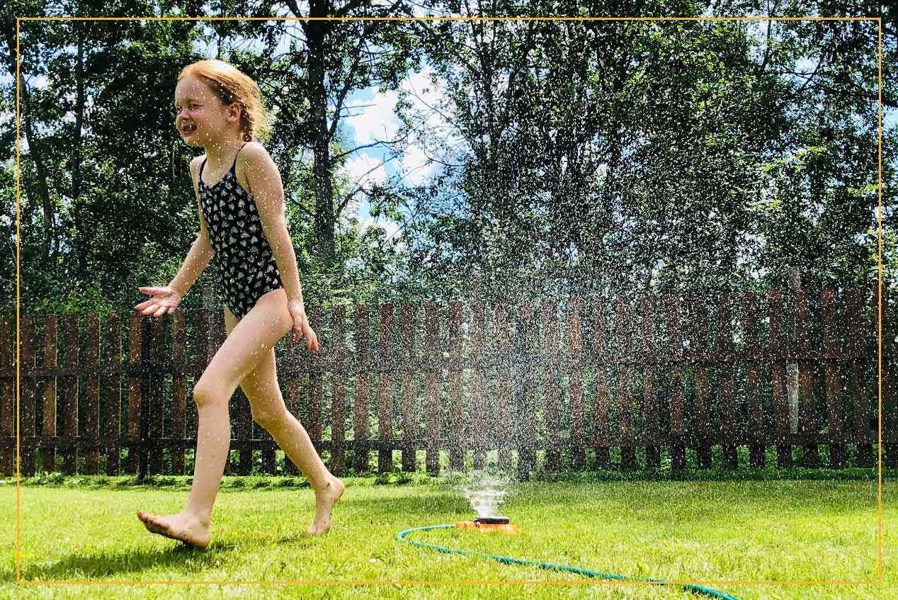 girl playing in backyard sprinkler