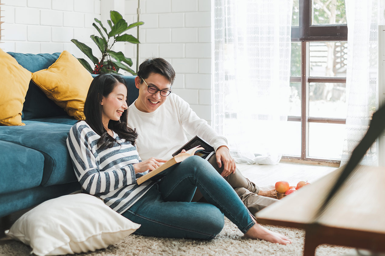 Couple read book while sitting on floor in house