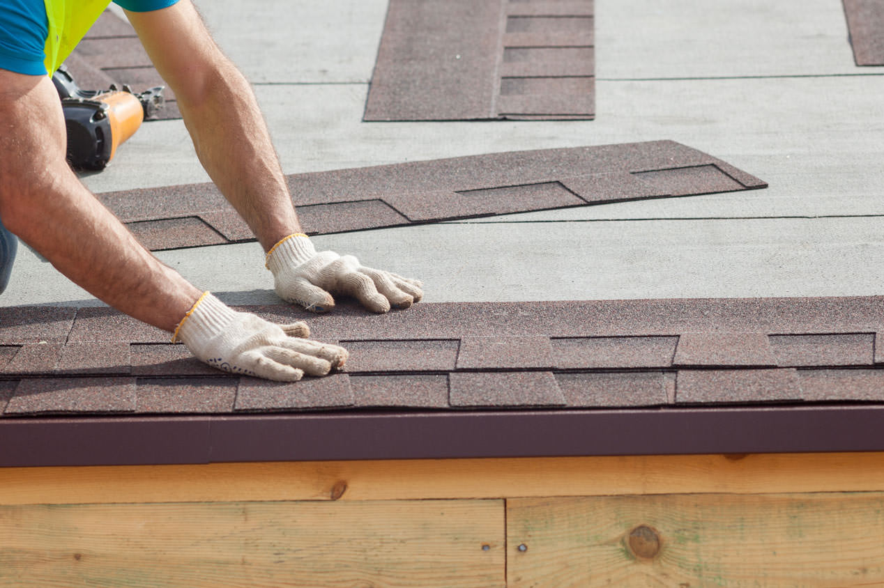 Detail of a worker’s hands in gloves installing new roof shingles