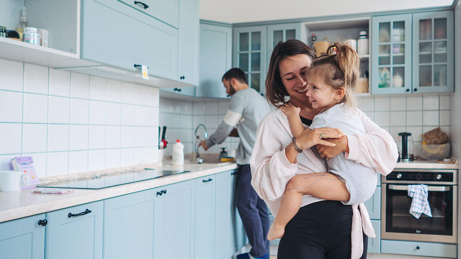 Mother standing in the kitchen is holding her daughter