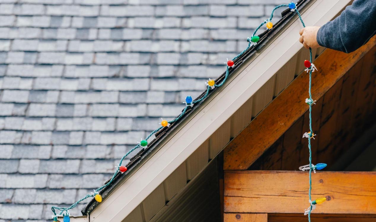 Man putting up holiday lights on roof edge